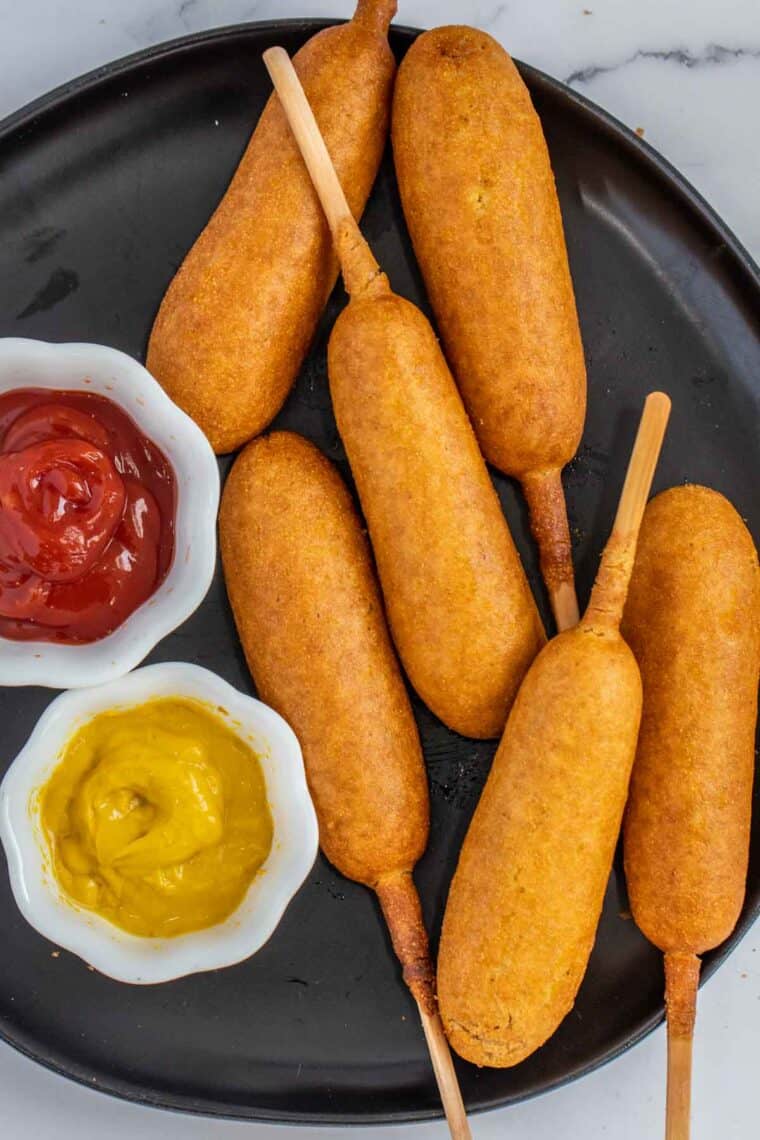 A black plate of corn dogs with ketchup and mustard. 