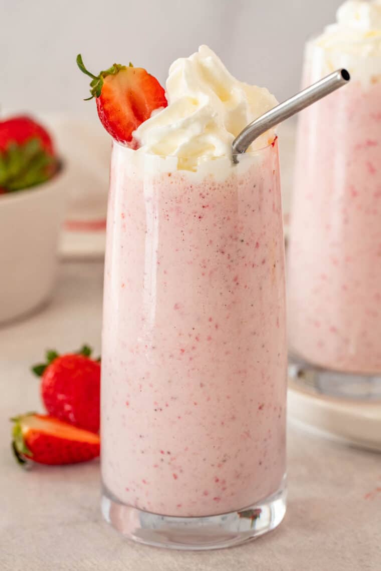 A glass of strawberry milkshake smoothie topped with whipped cream in a cup with a straw. 