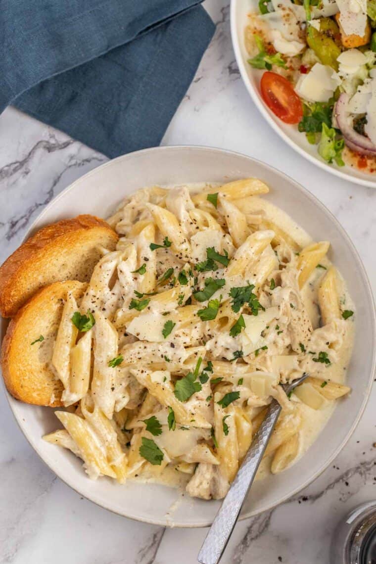 Chicken alfredo pasta on a white plate topped with fresh greens. 