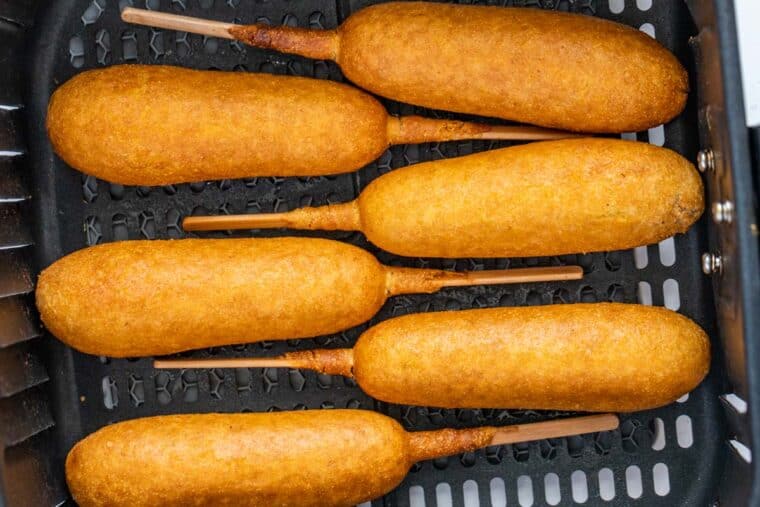 Corn dogs laid out in the air fryer basket. 