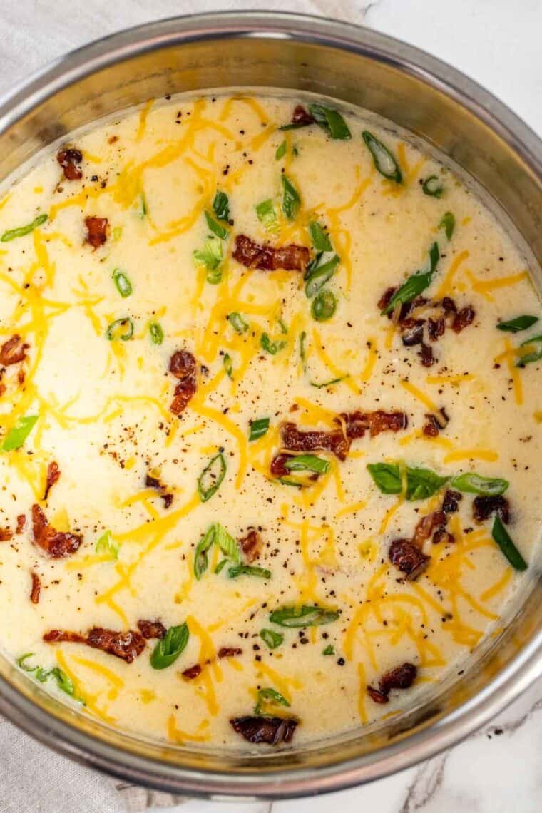 Creamy Potato Soup in an instant pot topped with green onions, bacon, and cheddar cheese.