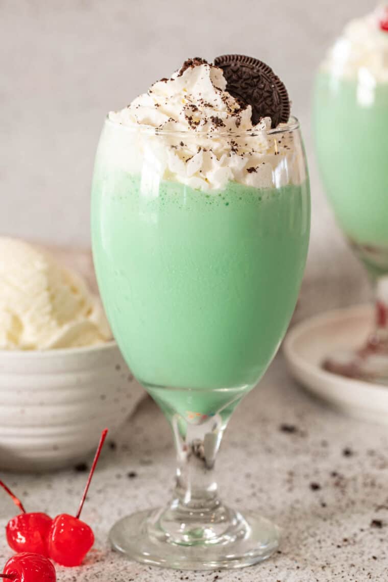 Shamrock shake in a glass cup topped with whipped cream and crushed oreos. 