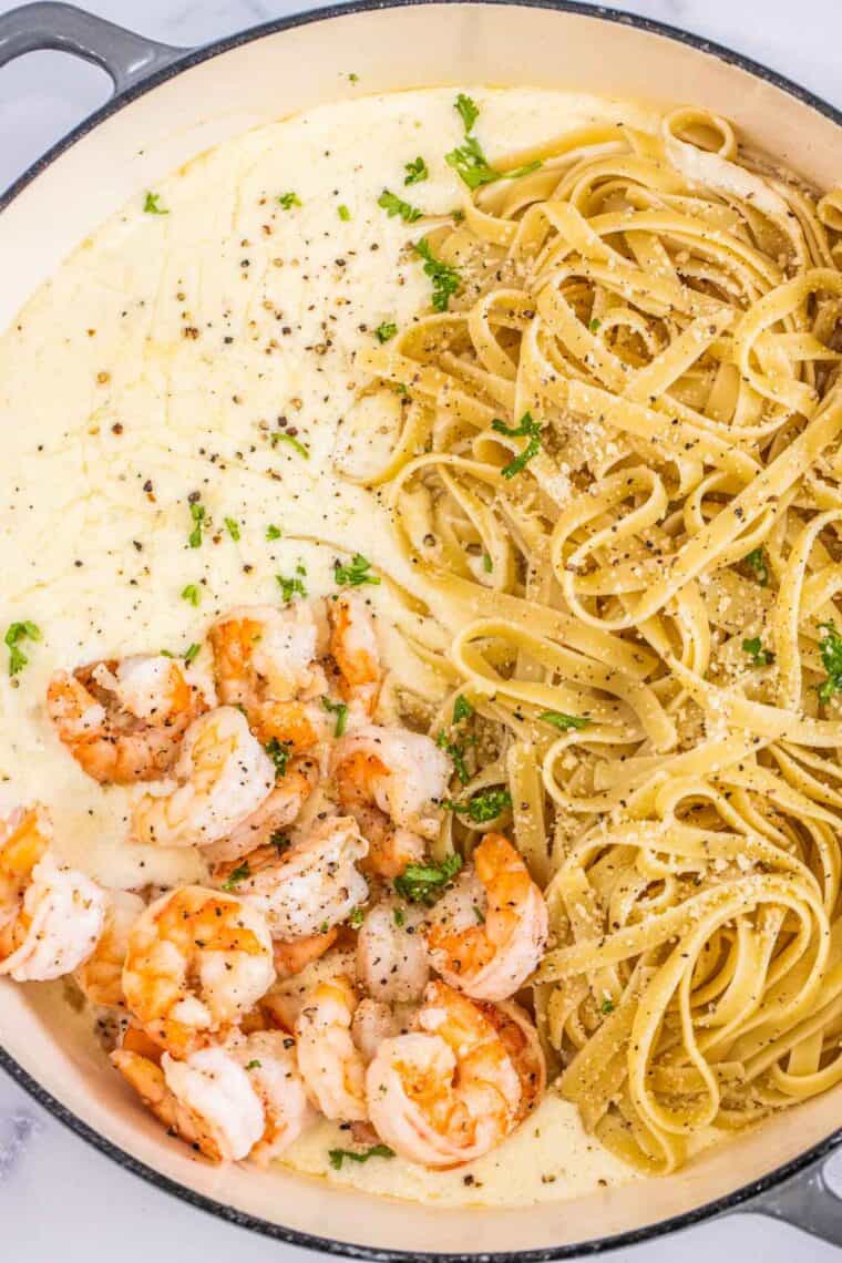 A deep skillet with Alfredo sauce, pasta and shrimp unmixed. 