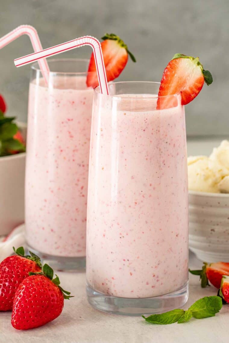 Homemade milkshake in glass cups next to fresh berries. 