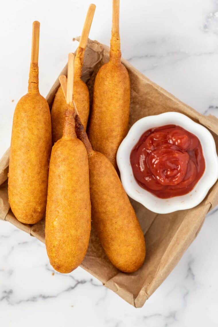 Corn dogs in a basket with a white bowl of ketchup. 