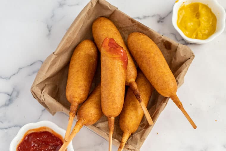 Air Fryer corn dogs in a brown basket with mustard and ketchup. 