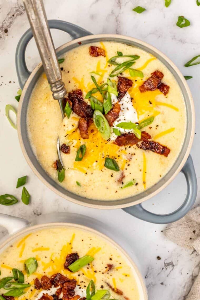 A bowl of potato soup with a metal spoon topped with sour cream, bacon, and green onion. 