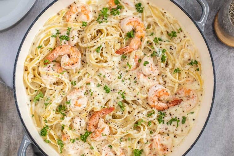 A deep skillet loaded with creamy fettuccine Alfredo pasta and shrimp. 