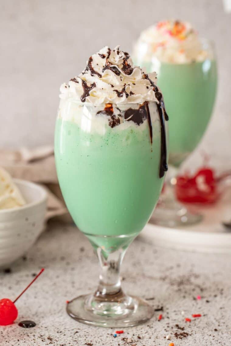 A glass of shamrock shake topped with whipped cream drizzled with chocolate syrup and crushed oreos. 
