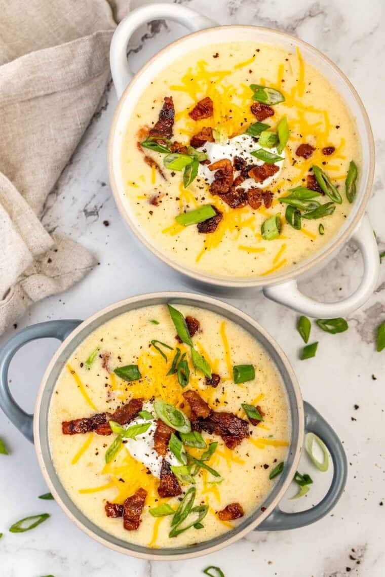 Two bowls of creamy potato soup loaded with toppings. 