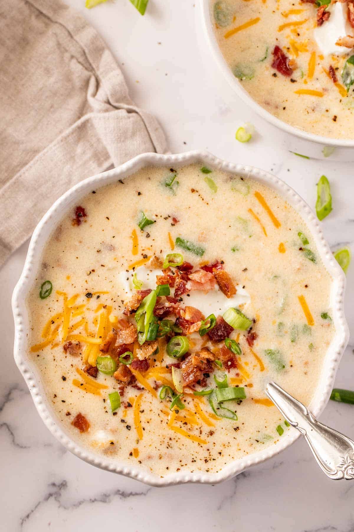 A bowl of slow cooker potato soup with a metal spoon and topped with toppings. 
