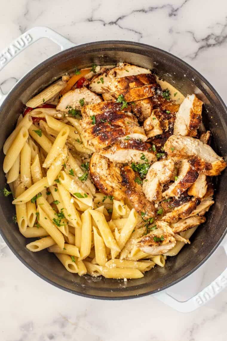 A white dutch oven with cooked pasta and sliced chicken for rasta pasta. 