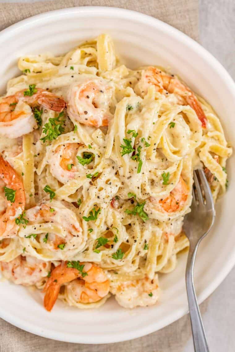 A white bowl of Shrimp Fettuccine Alfredo pasta topped with fresh parsley. 