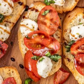 An open faced caprese bruschetta finger sandwich. Cherry tomatoes mixed with mozzerella cheese, basil, drizzled with balsamic glaze.