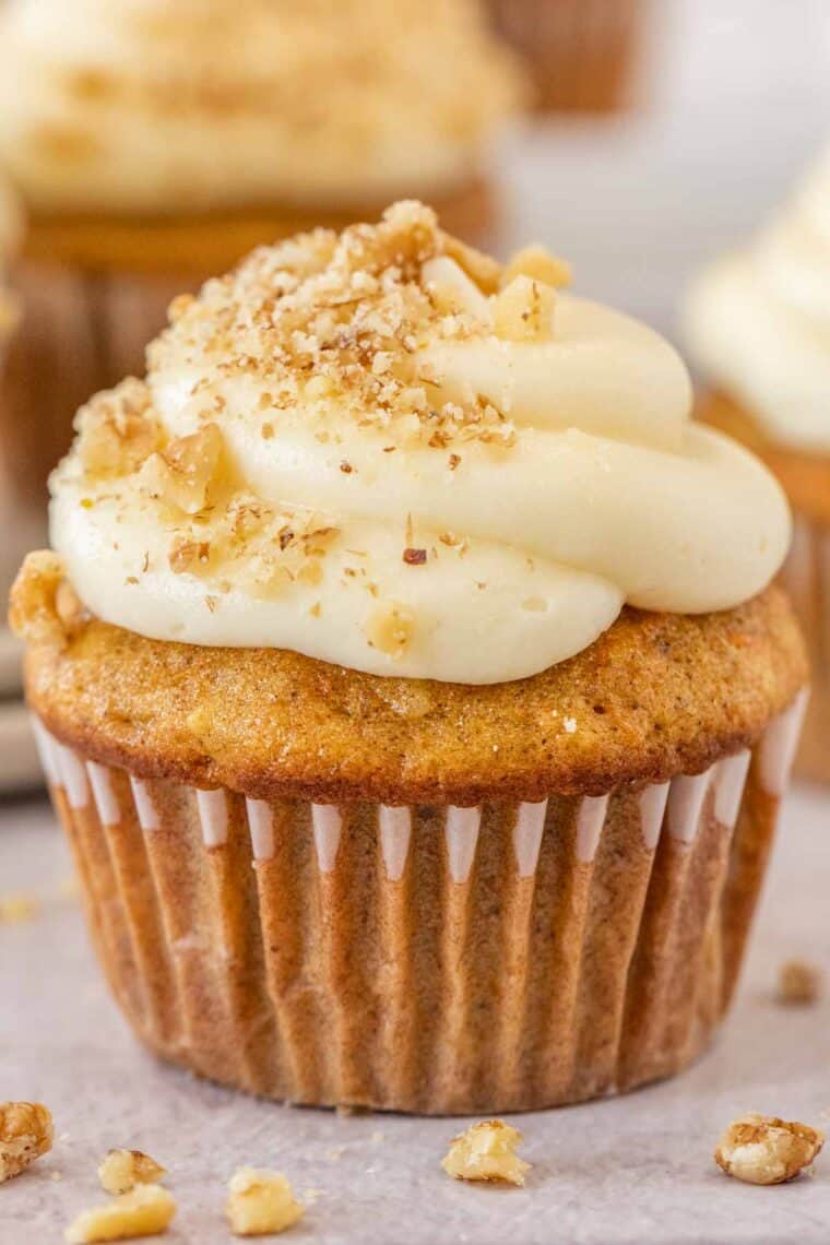 A carrot cake cupcake topped with cream cheese and chopped walnuts. 