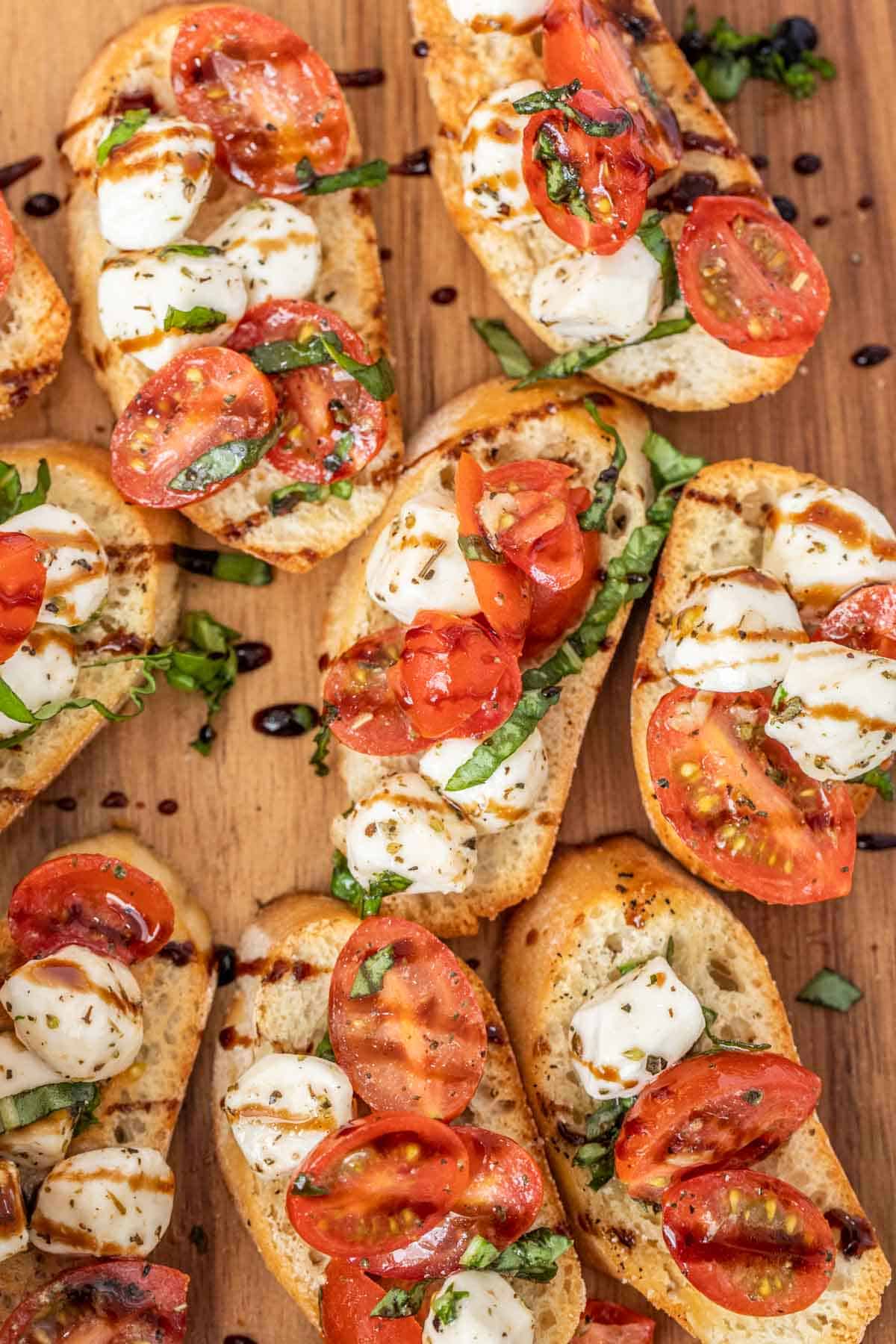 Homemade caprese bruschetta laid out on a cutting board drizzled with glaze. 