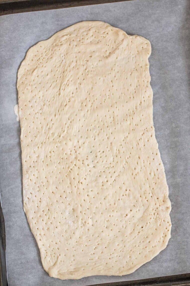 A baking sheet with parchment paper with flatbread dough. 