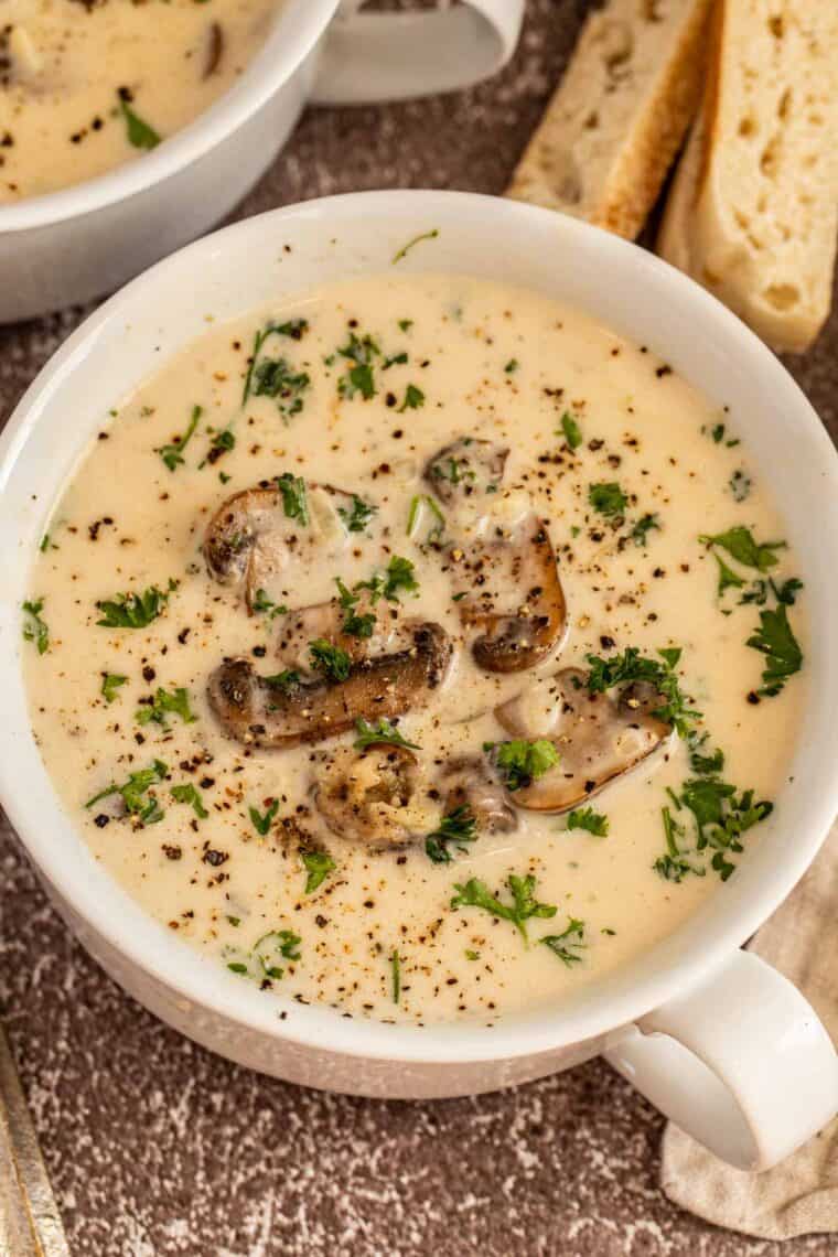 A white bowl of creamy mushroom soup topped with freshly chopped greens. 