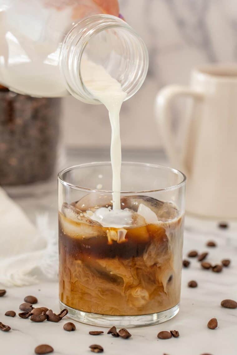 A glass cup with black coffee and creamer being poured into the cup. 