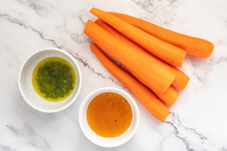 Whole carrots, garlic butter sauce or honey laid out. 