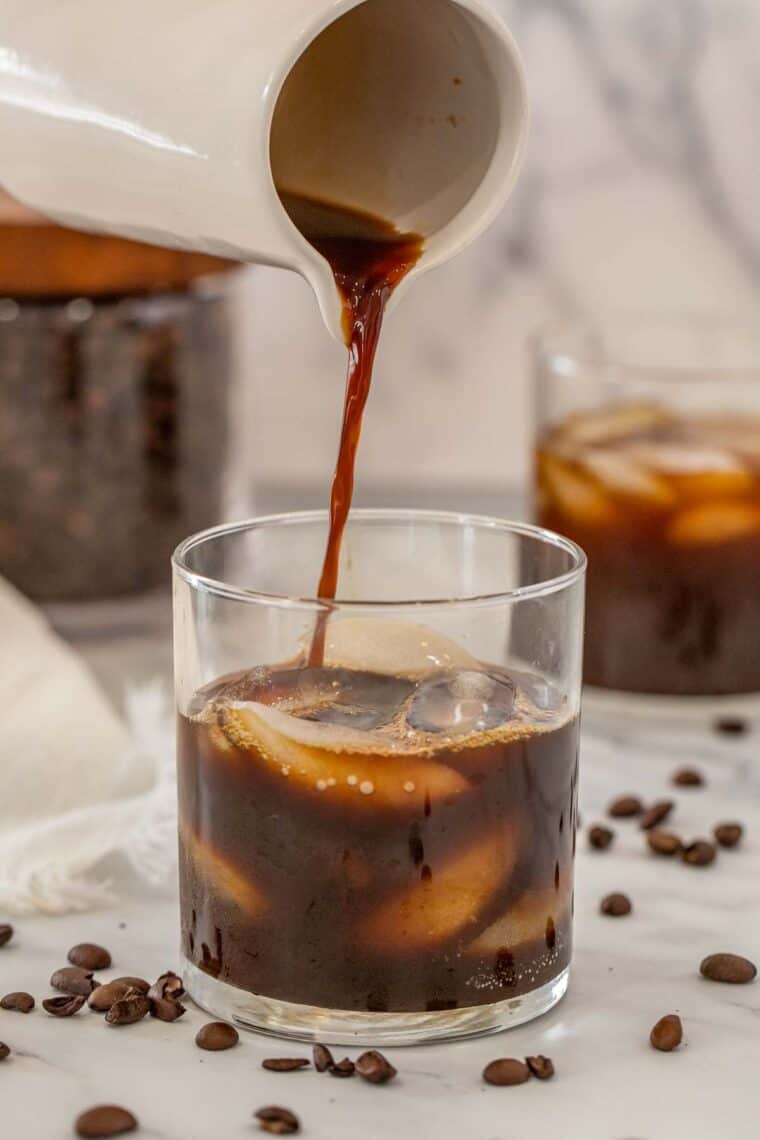 Black coffee being poured into a glass cup with ice.