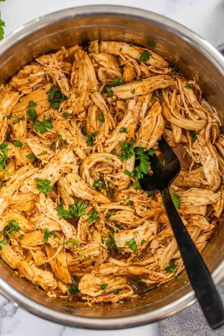 Juicy shredded chicken in the instant pot with a black fork topped with freshly chopped greens. 