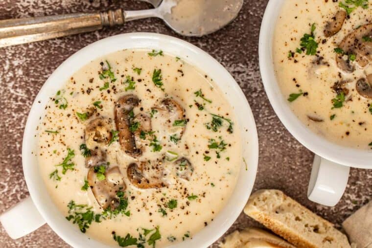 Two bowls of creamy mushroom soup topped with freshly chopped greens. 