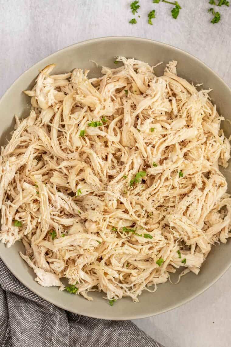 A gray plate of shredded chicken topped with fresh greens. 