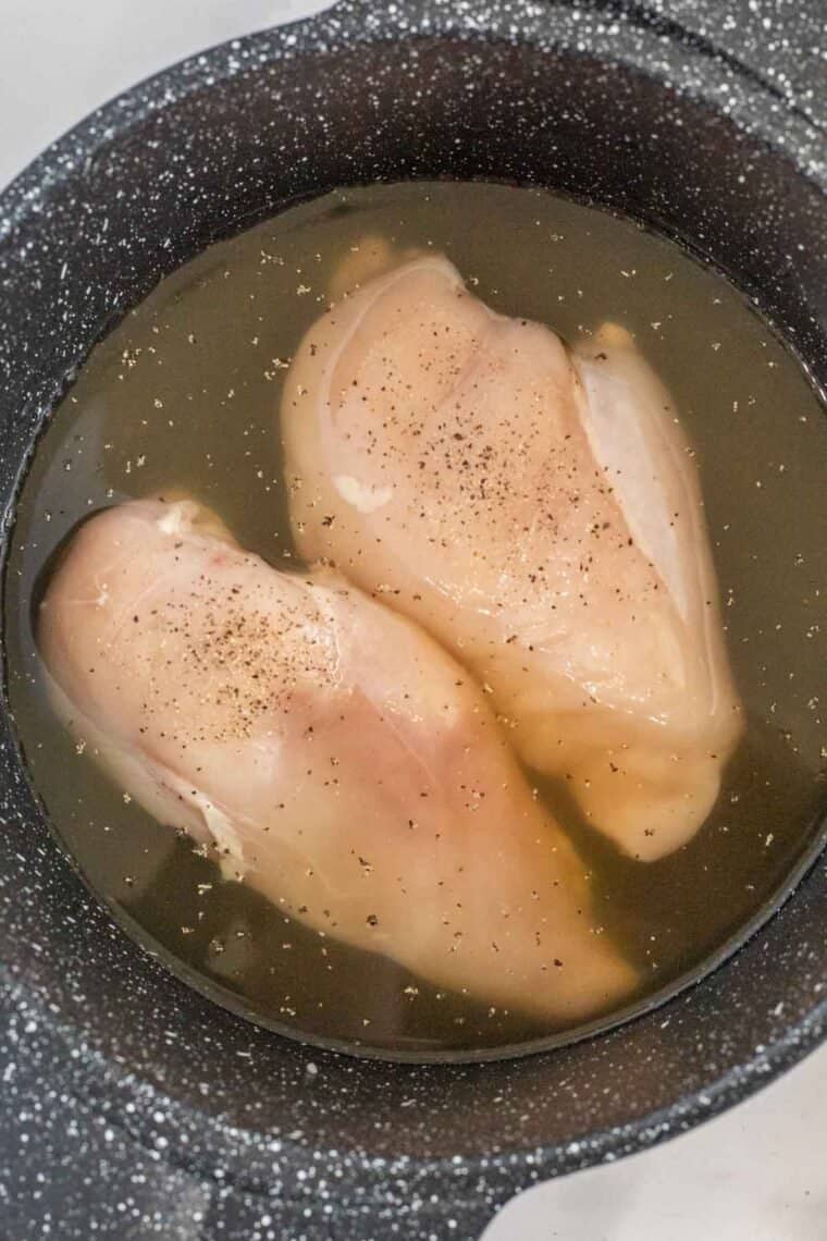 A black pot of chicken breast in broth, salt, and pepper. 
