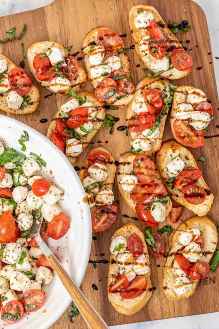 Bruschetta caprese laid out on a cutting board drizzled with glaze. 