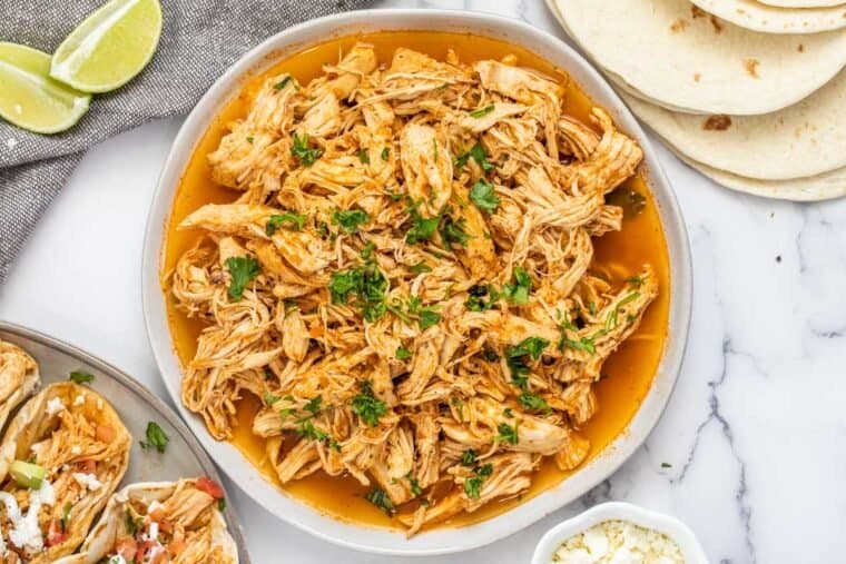 A white plate of shredded chicken topped with fresh chopped greens, 