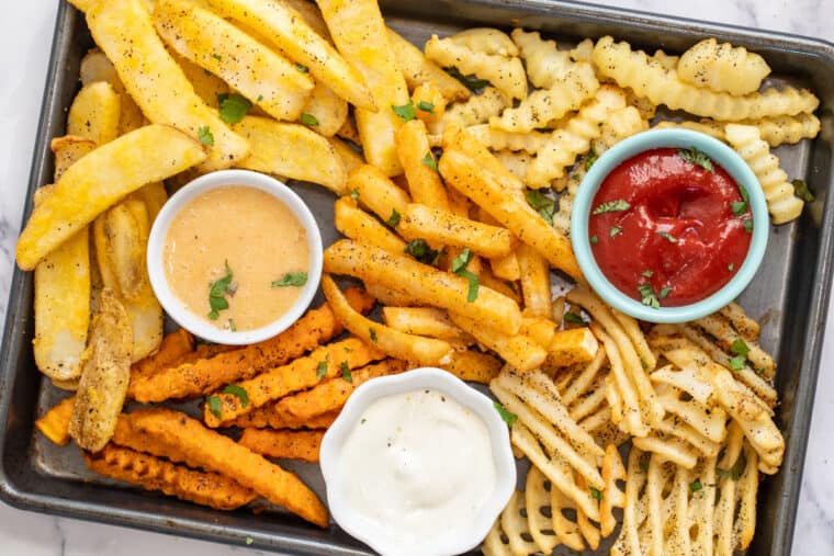 A baking sheet with crispy french fries with three different dipping sauces. 