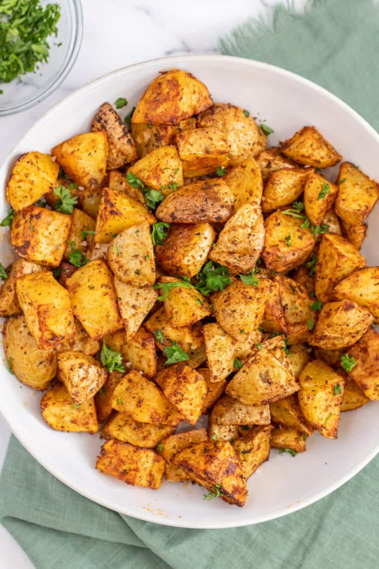 A white plate with crispy air fryer breakfast potatoes topped with cilantro  and black pepper.