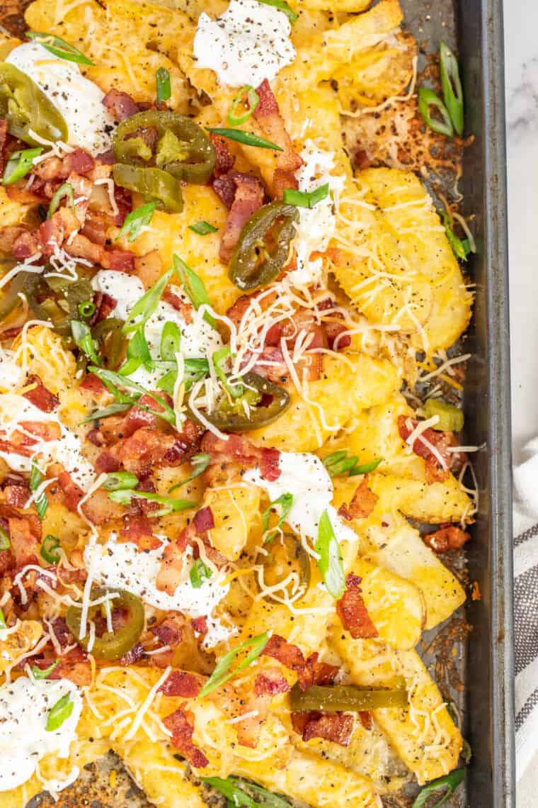 Loaded cheese fries topped with fresh greens on a baking sheet. 