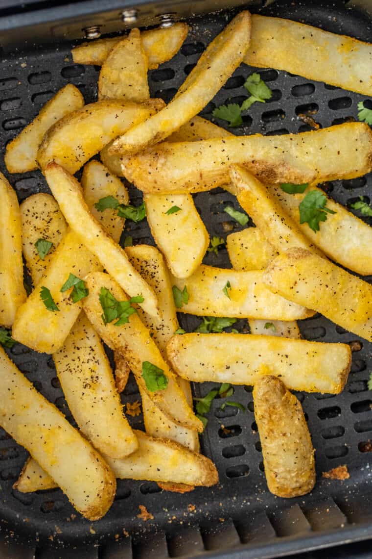 Crunchy french fries in the air fryer basket topped with fresh chopped greens. 