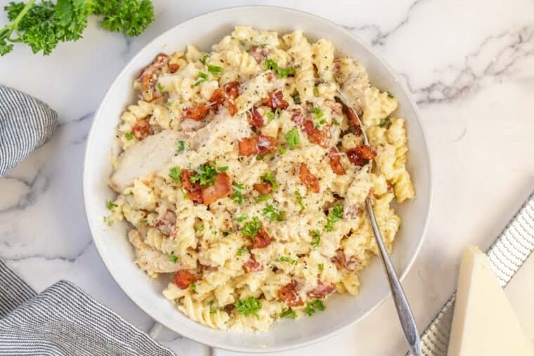 A plate of chicken bacon ranch pasta with a metal spoon topped with parsley. 