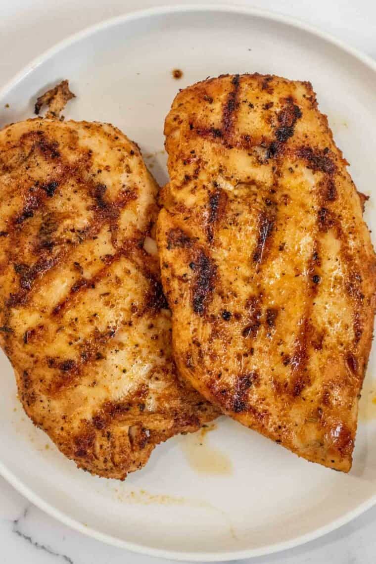 A white plate with grilled chicken. 