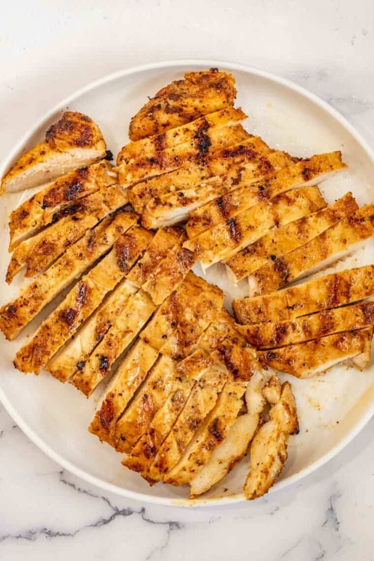 Marinated chicken breast sliced into pieces with a white plate. 