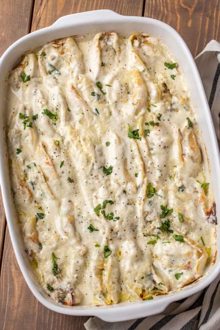 Creamy stuffed shells in a white casserole dish topped with fresh chopped greens and black pepper. 