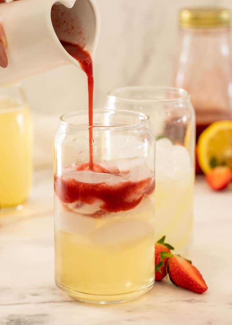 Glass cups with lemonade and strawberry acai syrup being poured into the cups. 