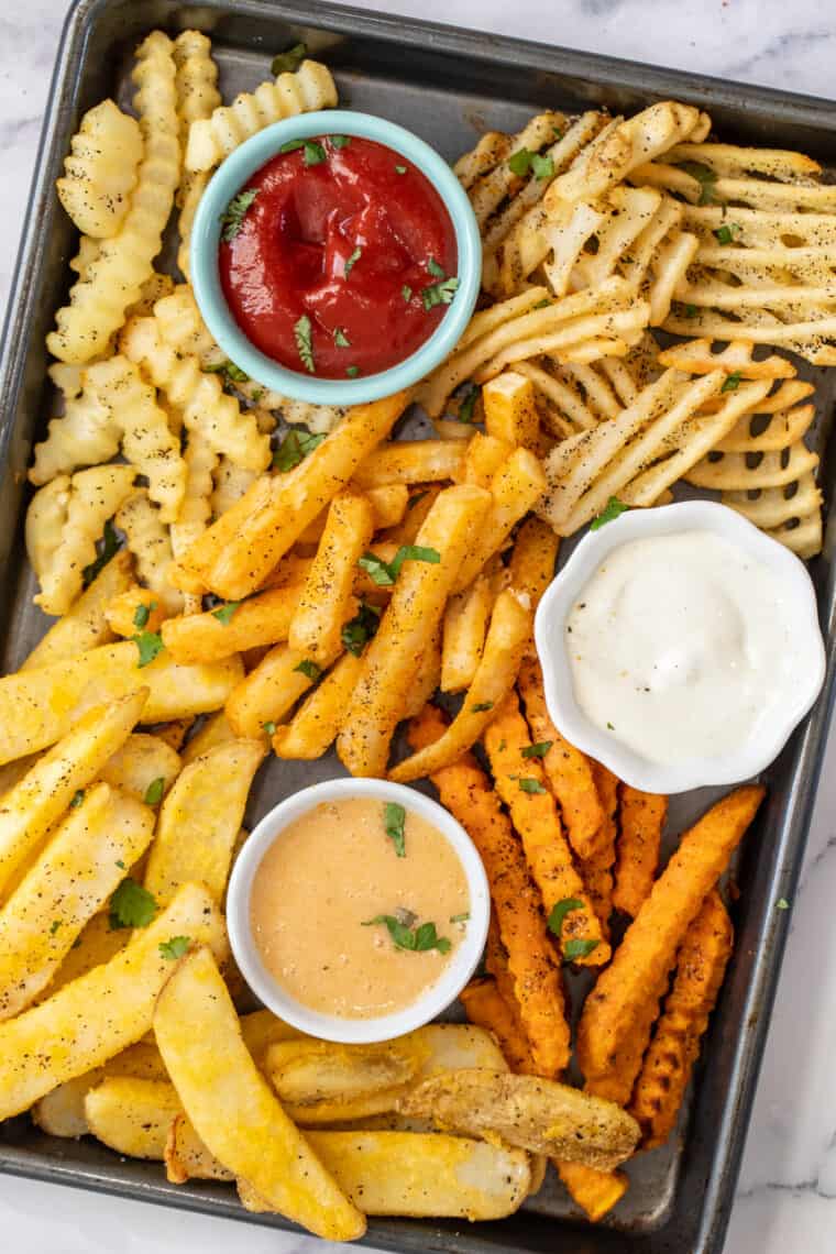 A baking sheet of french fries and dipping sauces. 