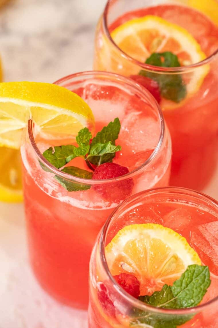 Three glasses of raspberry lemonade with lemon slices and mint. 