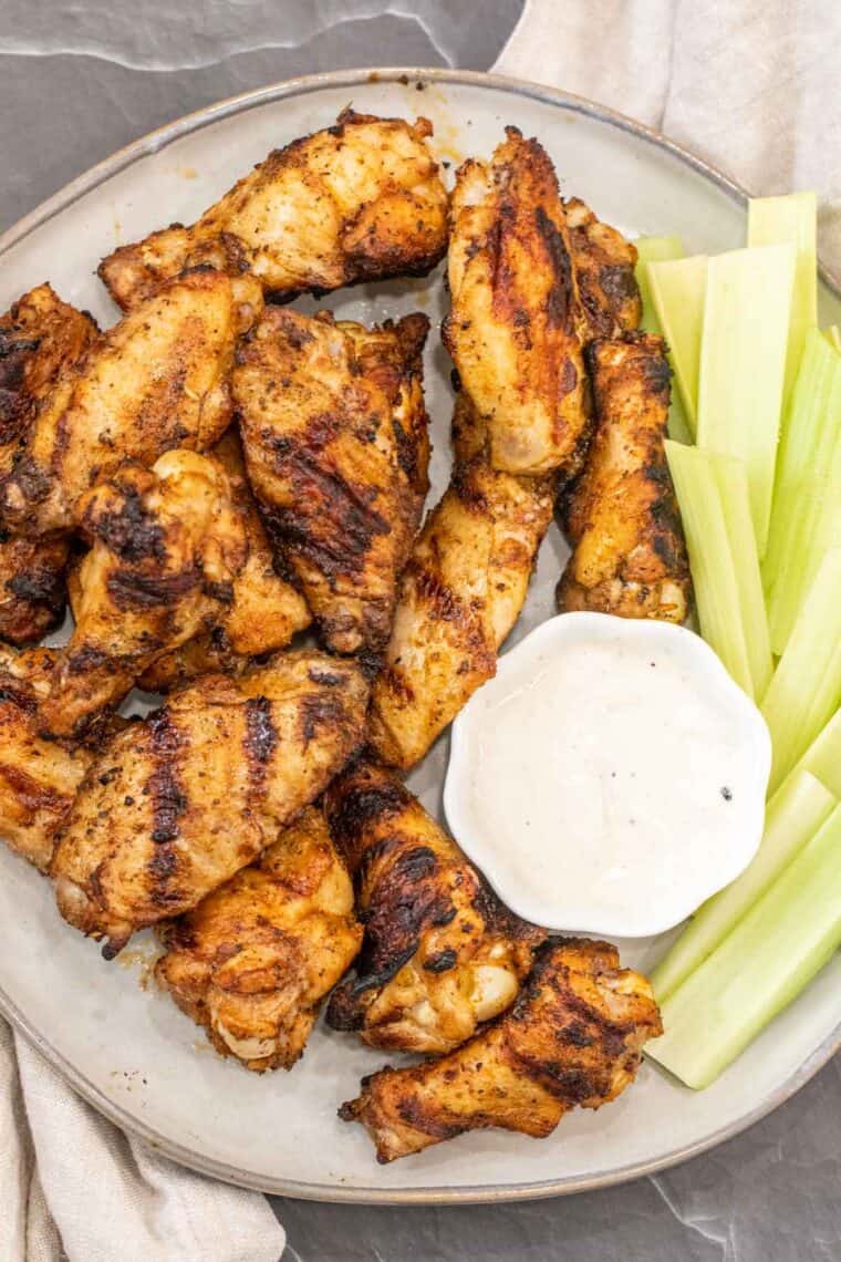 Crispy grilled chicken wings on a plate with celery and ranch dressing. 
