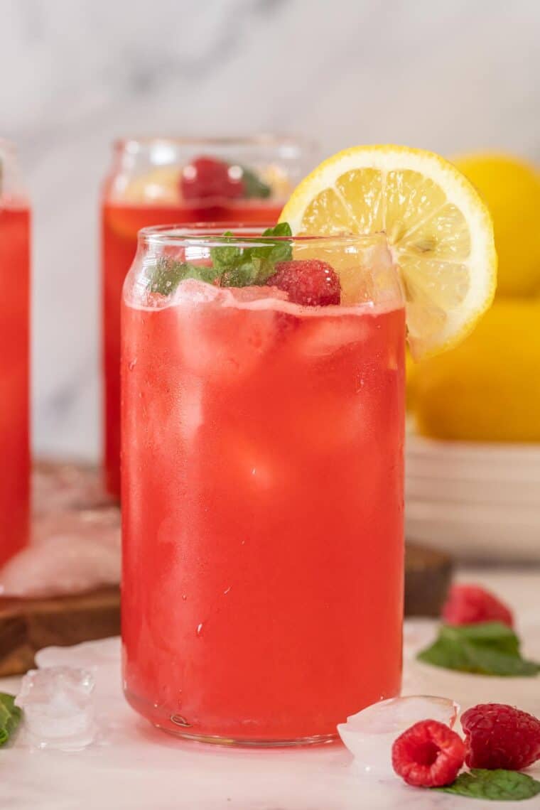 A glass of lemonade with a lemon slice and fresh raspberries. 