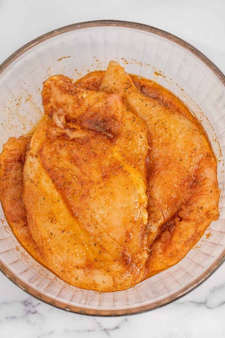 A glass bowl of chicken in the marinade mixture. 