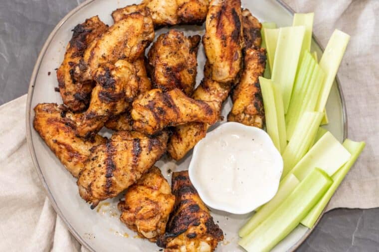 Grilled chicken wings on a plate with celery sticks and Ranch dressing. 