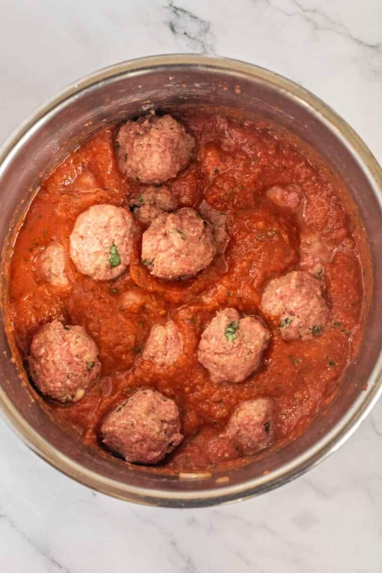 Uncooked meatballs in the instant pot with sauce ready to be cooked. 