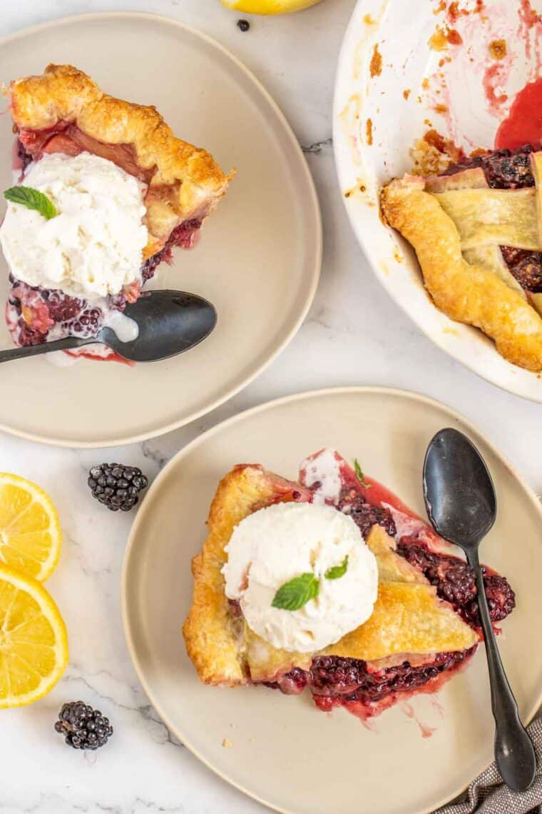 Blackberry pie slices on two plates with black spoons. 