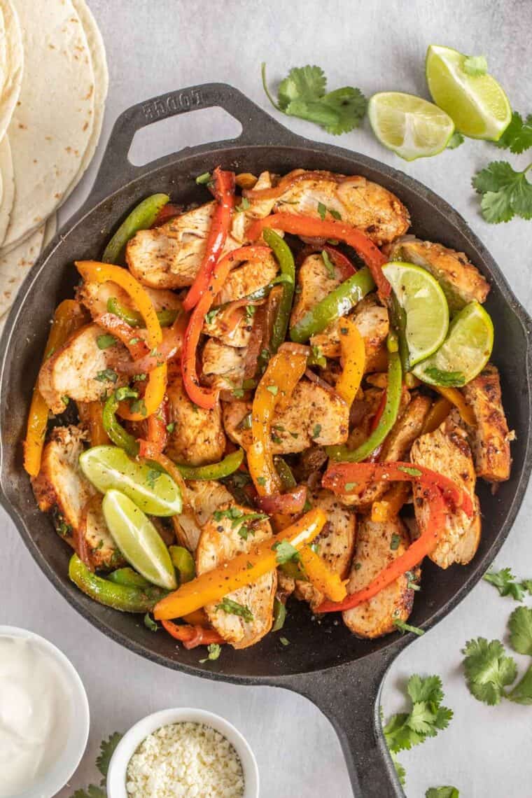Black cast iron dish loaded with chicken fajitas topped with fresh chopped greens. 