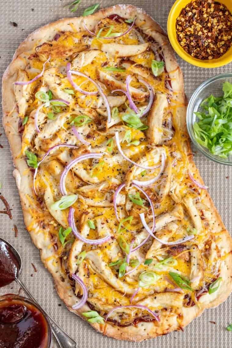 BBQ chicken flatbread on a baking sheet topped with green onion. 
